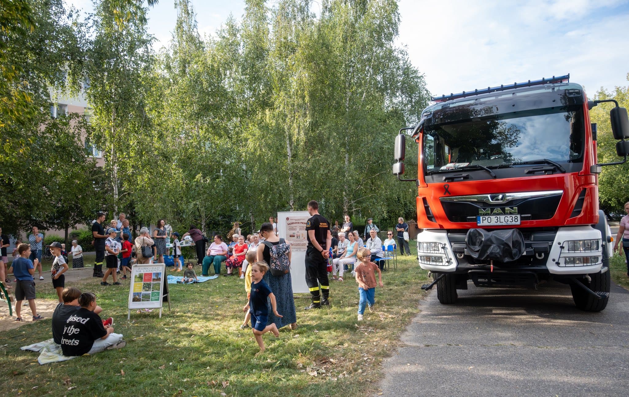 Wóz strażacki i mieszkańcy na terenie zielonym podczas pikniku