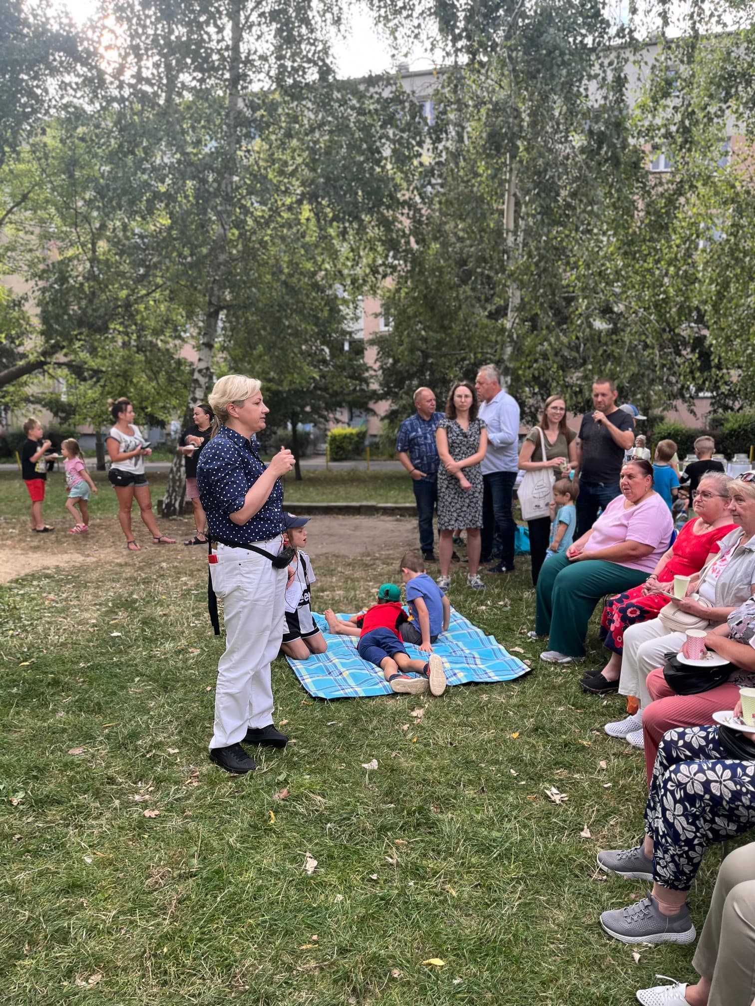 Prowadząca rozmawia z mieszkańcami podczas spotkania na trawie