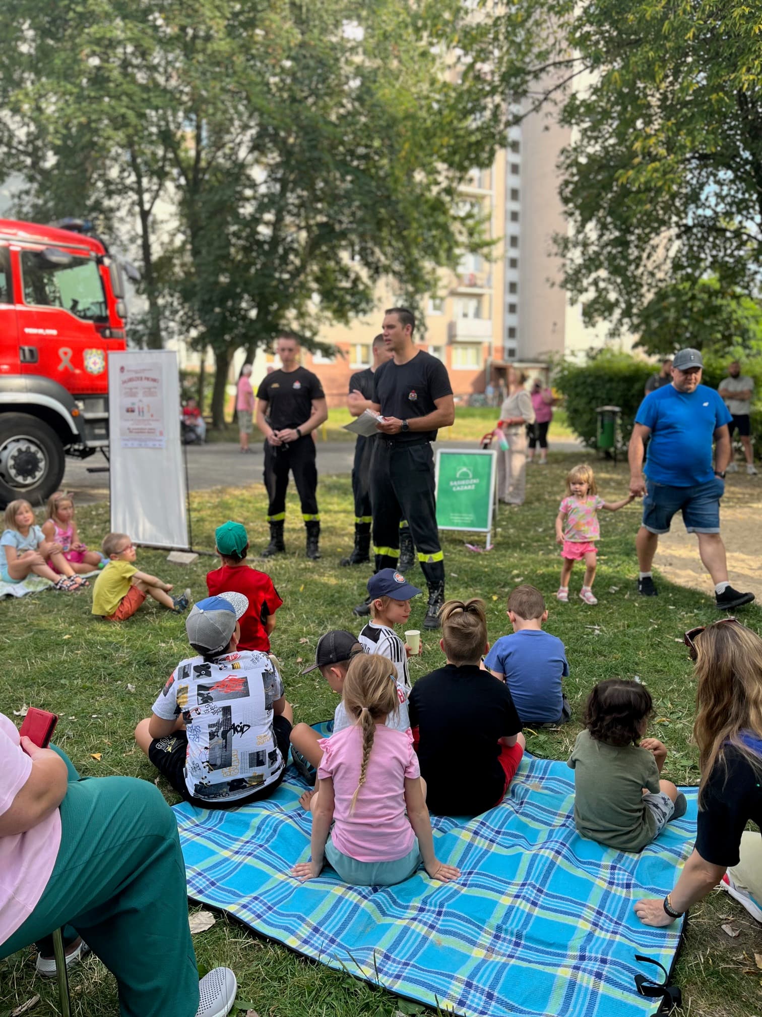 Dzieci i rodzice słuchają strażaków podczas pokazu bezpieczeństwa